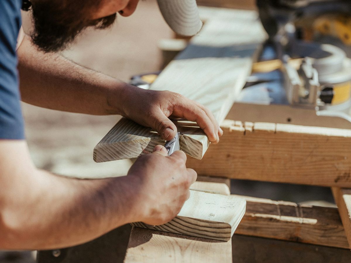 Hände bearbeiten ein Holzbrett an der Werkbank