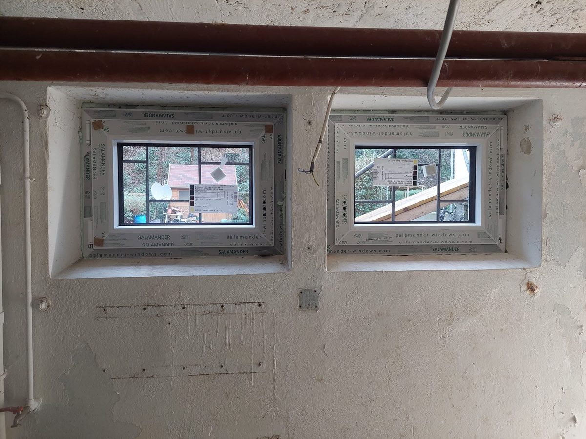 Zwei neu eingebaute Kellerfenster in einer verputzten Wand