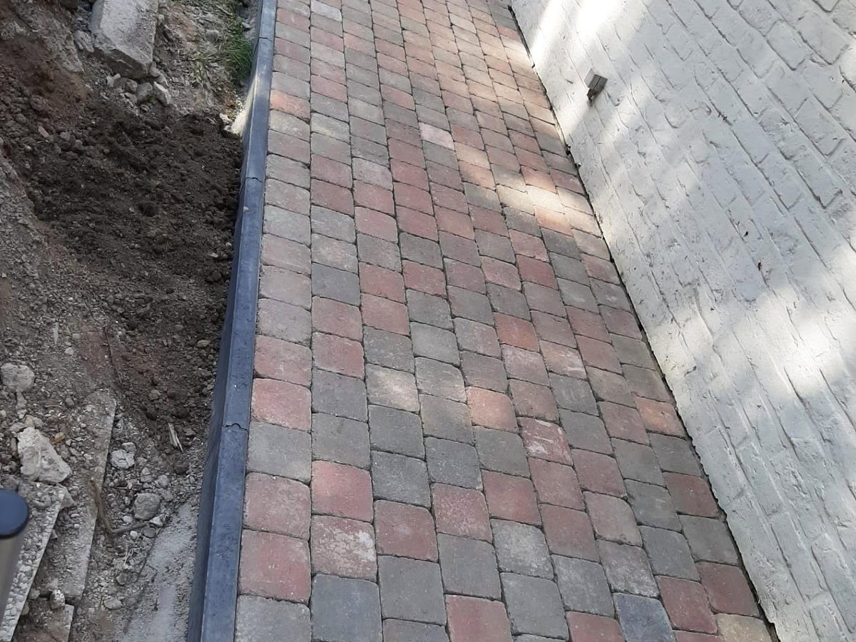 Fertig gepflasterter Weg mit Randsteinen entlang einer weißen Backsteinwand