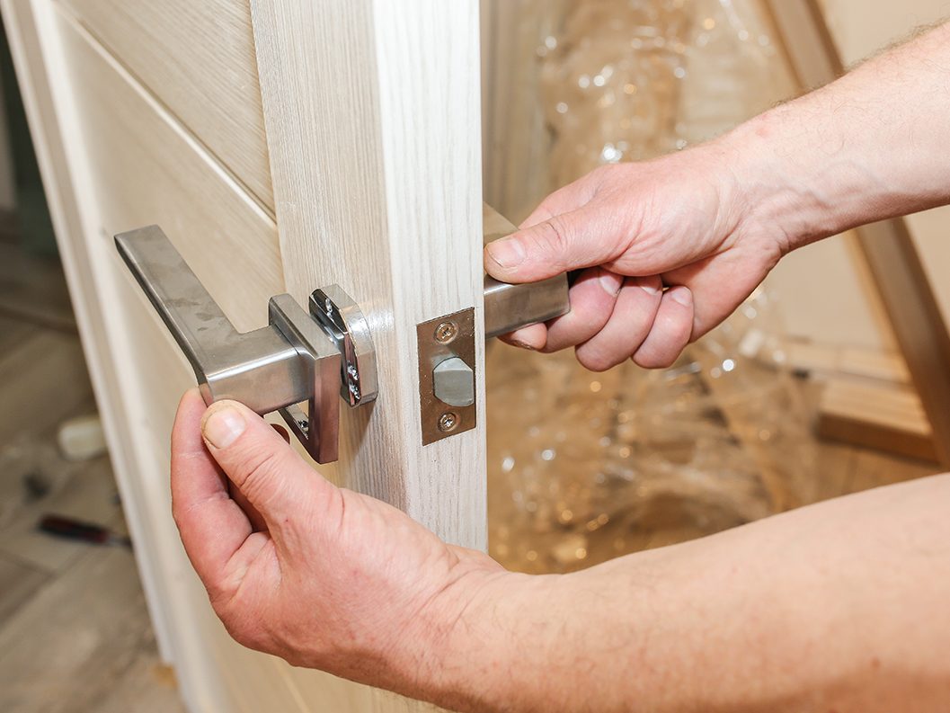 Hände montieren eine Holztür und setzen den Türgriff aus Metall ein